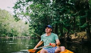A man paddling a canoe along Pine Creek, with creek banks in distance. Photo: Jay Black © OEH