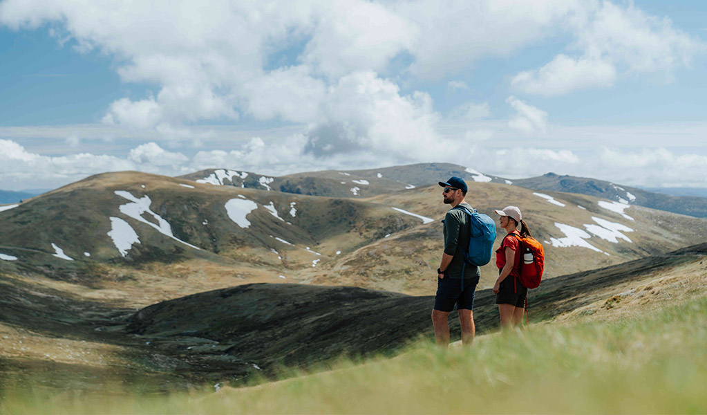 2 hikers looking out at mountain views from Rawson Pass on Snowies Alpine Walk in the Thredbo-Perisher area of Kosciuszko National Park. Credit: Remy Brand / DCCEEW &copy; Caravel Content