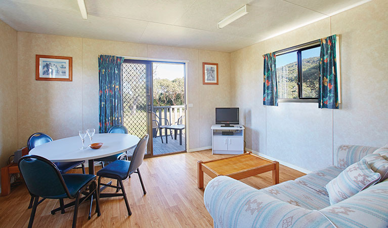The dining and lounge room with dining table, couch and TV in Pretty Beach cabins, Murramarang National Park. Photo: Nick Cubbin &copy; DPIE