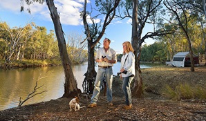 A couple and their dog next to the Murrumbidgee River with a tent in the background at Wooloondool campground, Murrumbidgee Valley Regional Park. Photo: Gavin Hansford © DPIE